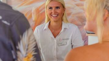 A person in a white shirt with a name tag, standing in a room with a glass partition and a poster in the background.
