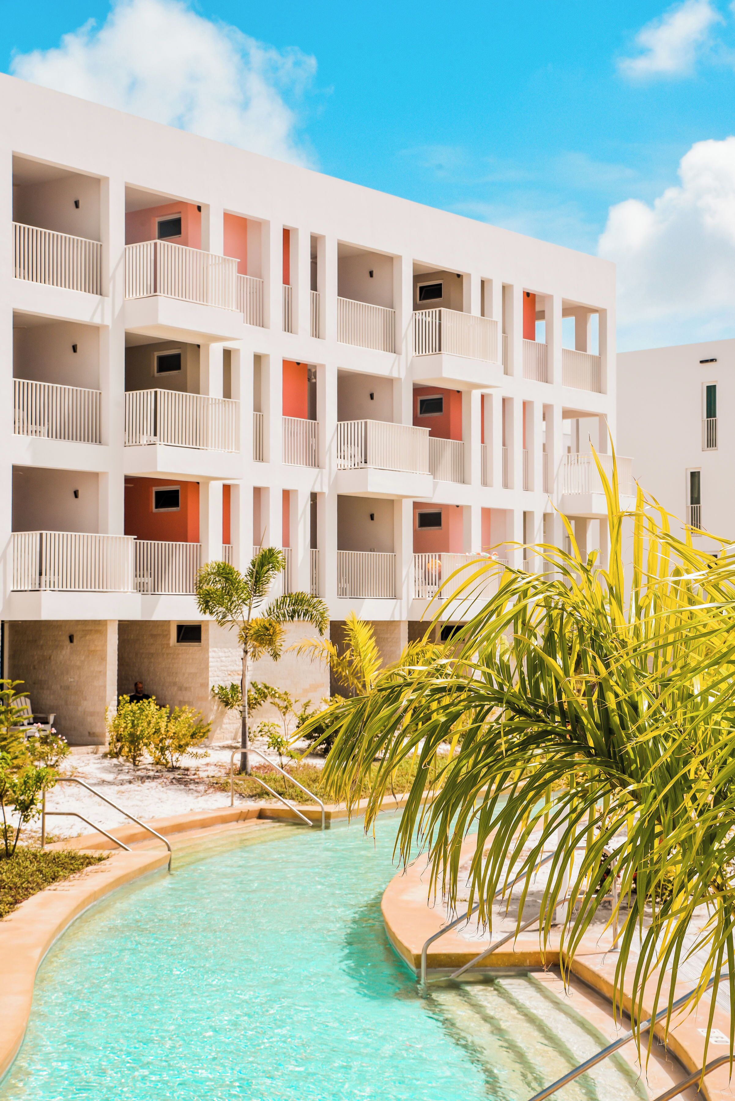 Un hotel de varios pisos con balcones, piscina y jardines tropicales.