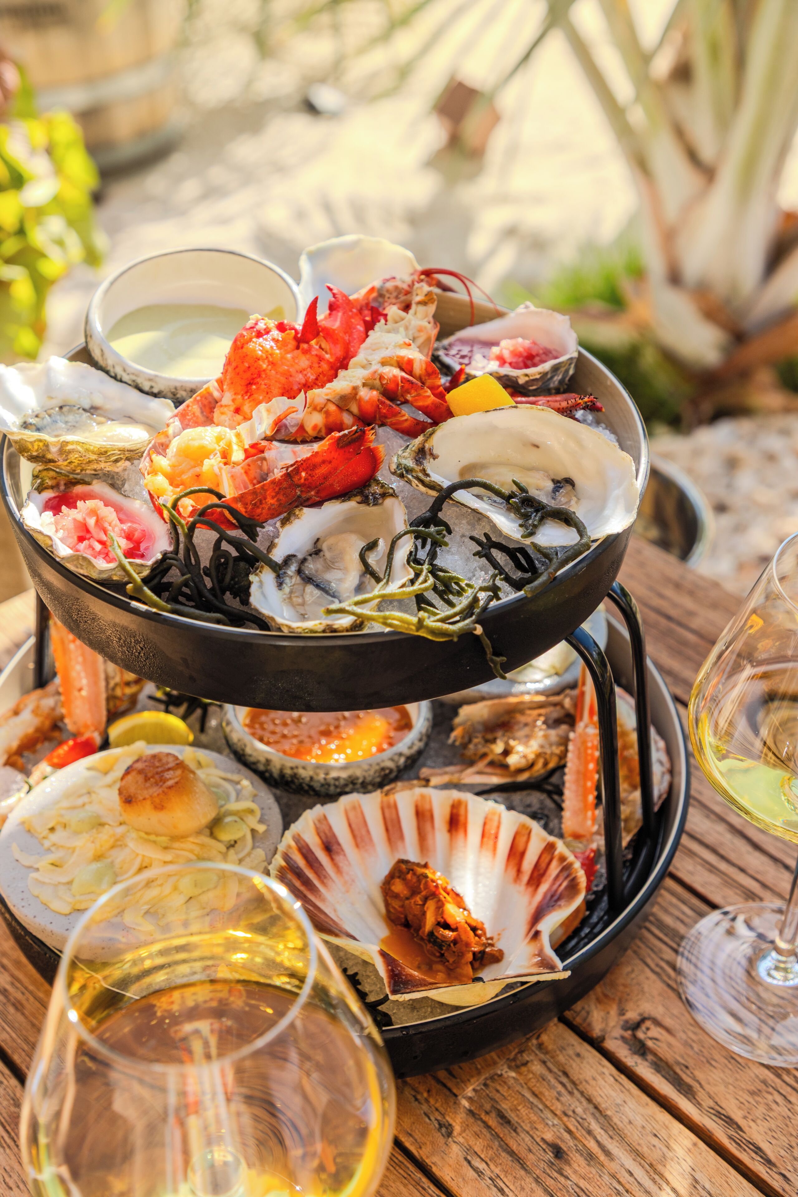 A seafood platter with various shellfish and a glass of white wine on a wooden table.