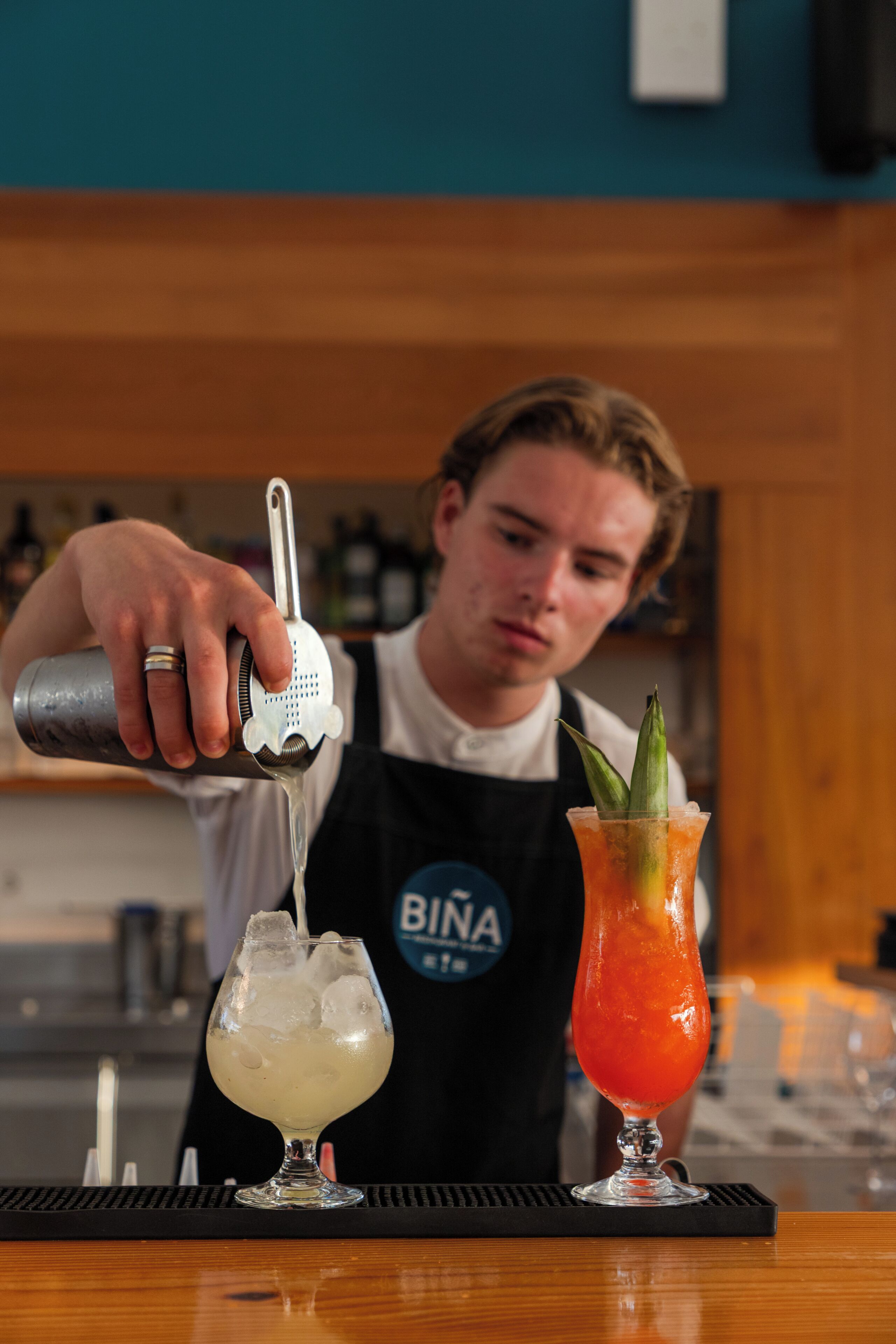 A bartender pouring a drink into a glass with a metal jigger.
