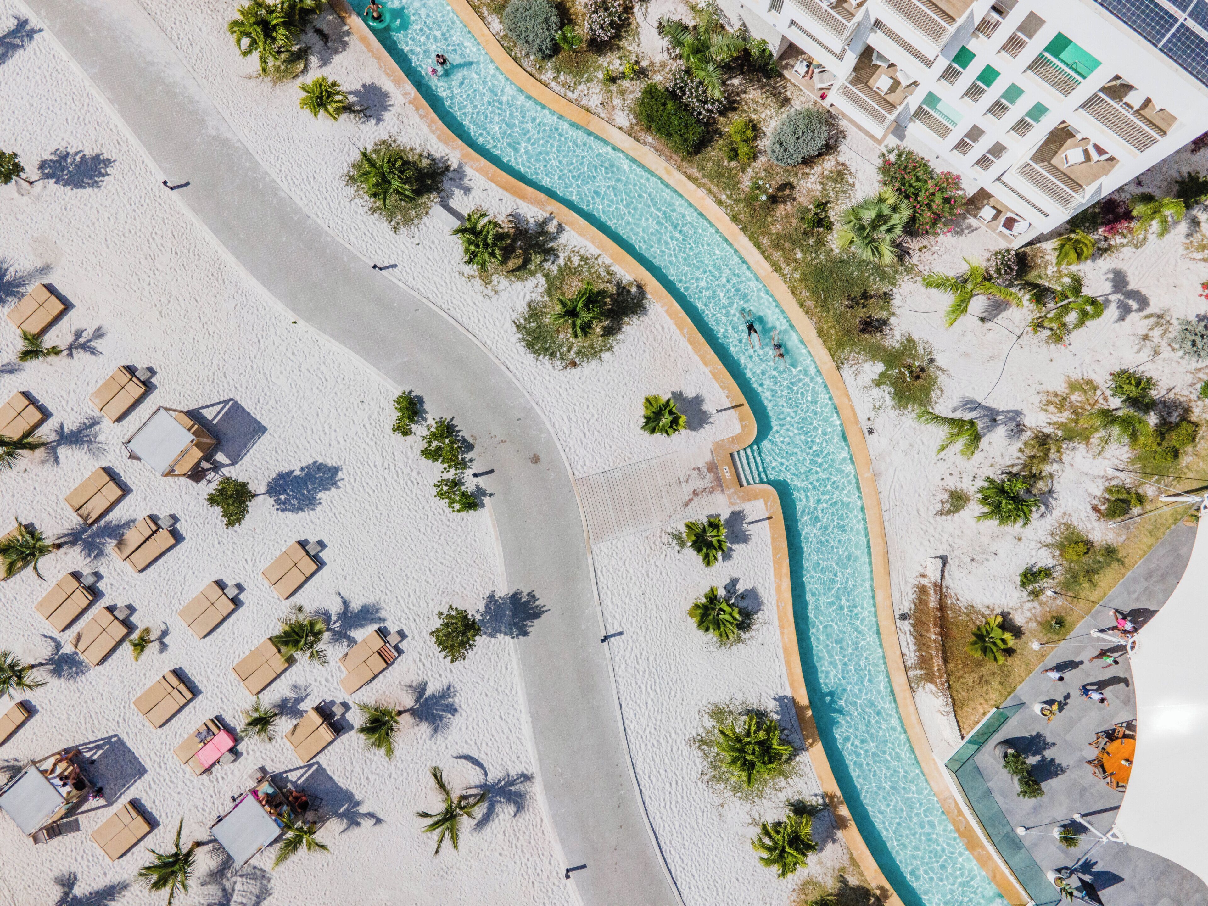 Vista aérea de um resort à beira-mar, com piscina, espreguiçadeiras e palmeiras.