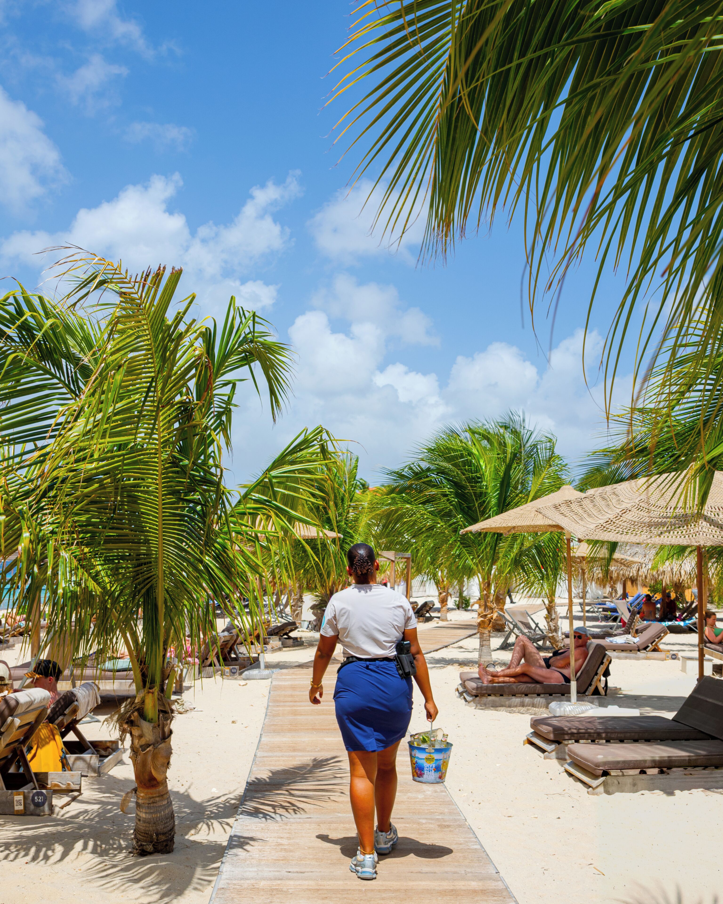 Un sentier bordé de palmiers menant à des espaces aménagés pour se détendre au bord de la plage.