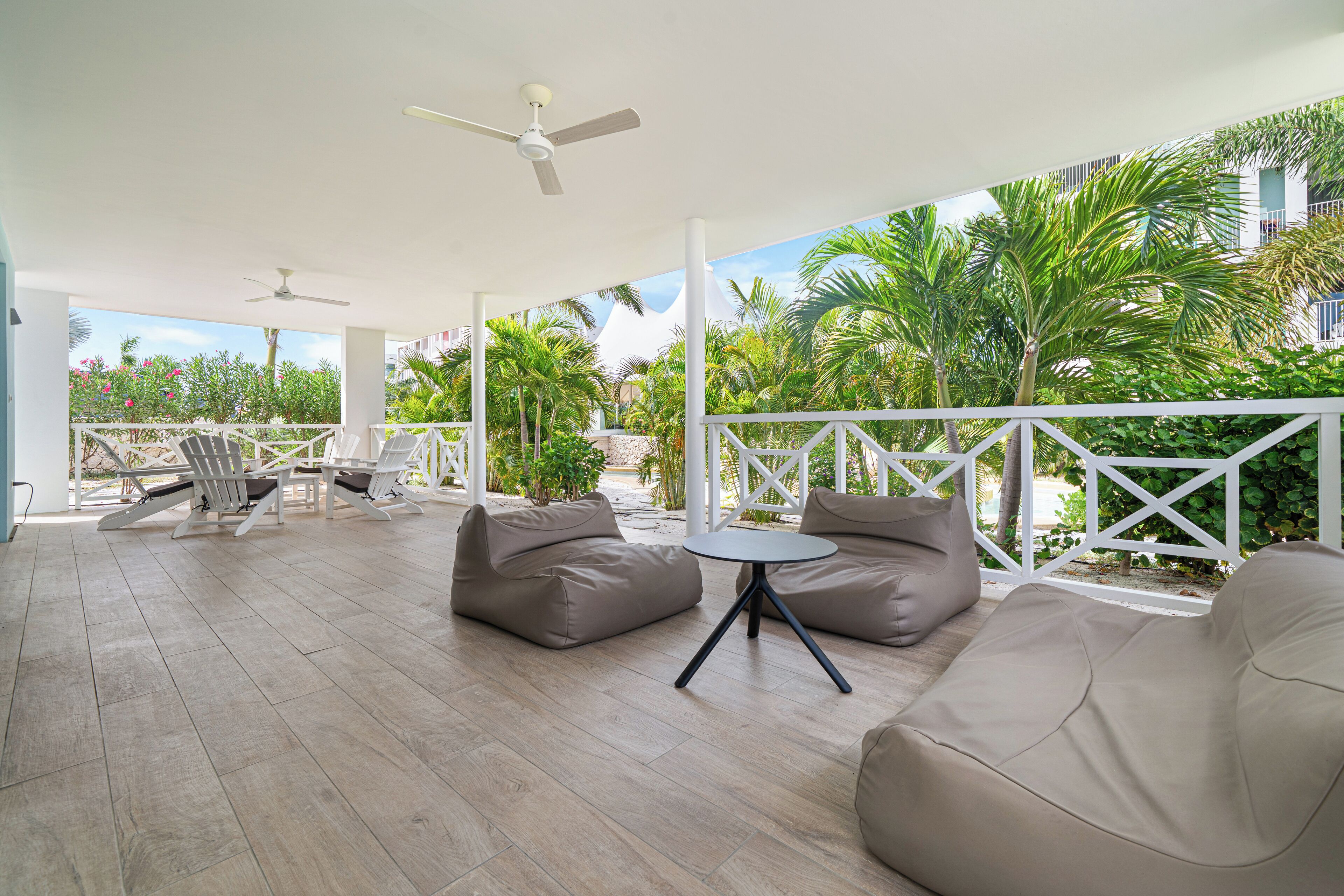 Un patio exterior con sofás color beige, una mesa redonda y ventiladores de techo.