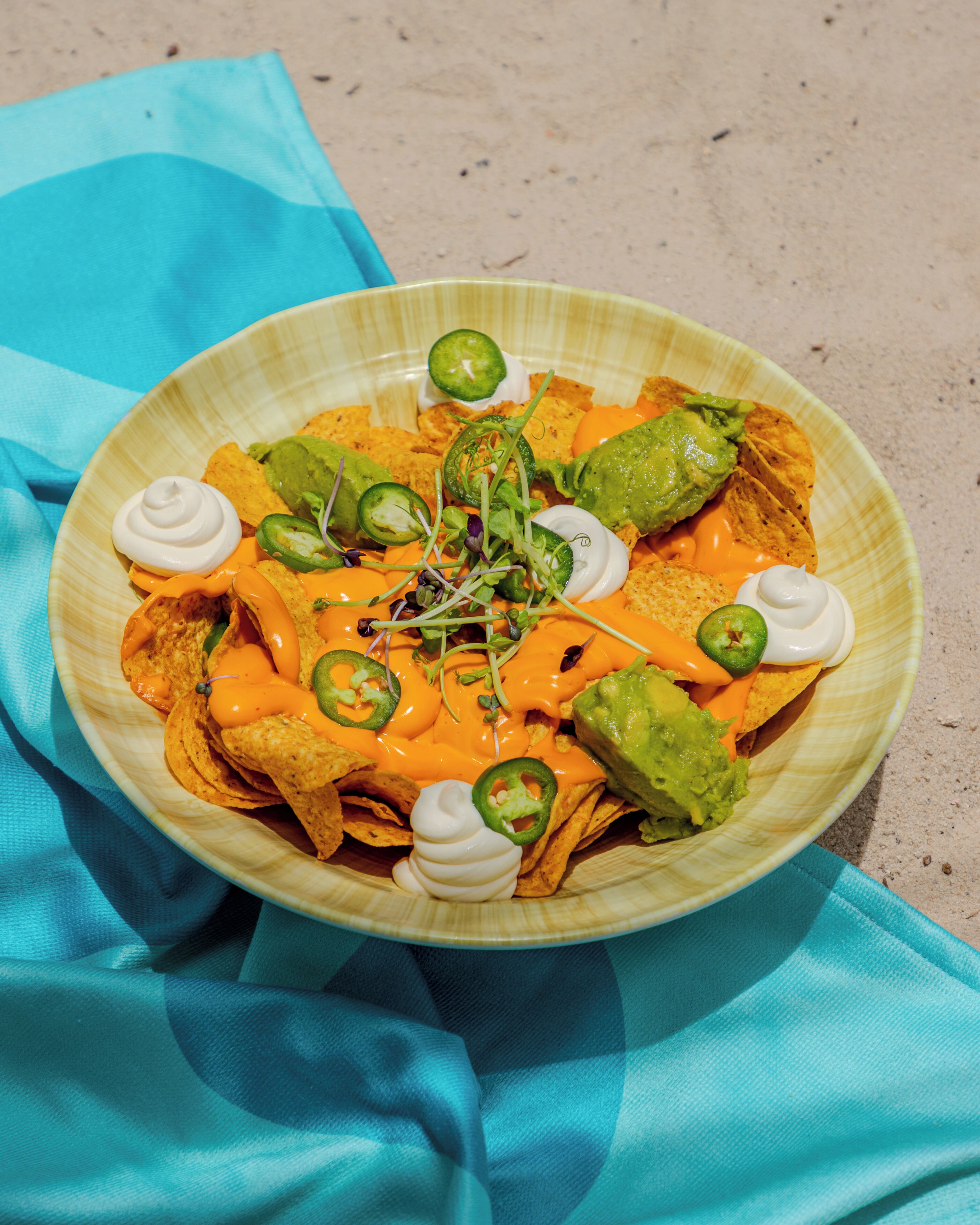 Een bord nachos met toppings, op een strand.