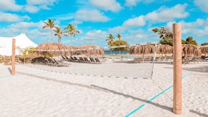 Een strandvolleybalveld met een net, omringd door ligbedden en palmbomen.