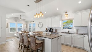 A modern kitchen with white cabinetry, a central island with bar stools, and pendant lighting. - Awesome 5 bed, 5 bath, heated pool - short walk to the beach! (Surf City)