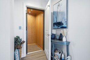 Een gang met een houten deur die naar een kamer leidt, een aan de muur hangend schilderij en een console tafel met decoratieve objecten.