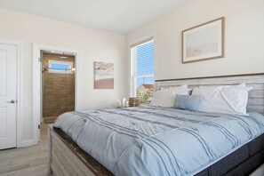 A bedroom with a bed, a door, a window, and a wall-mounted picture.