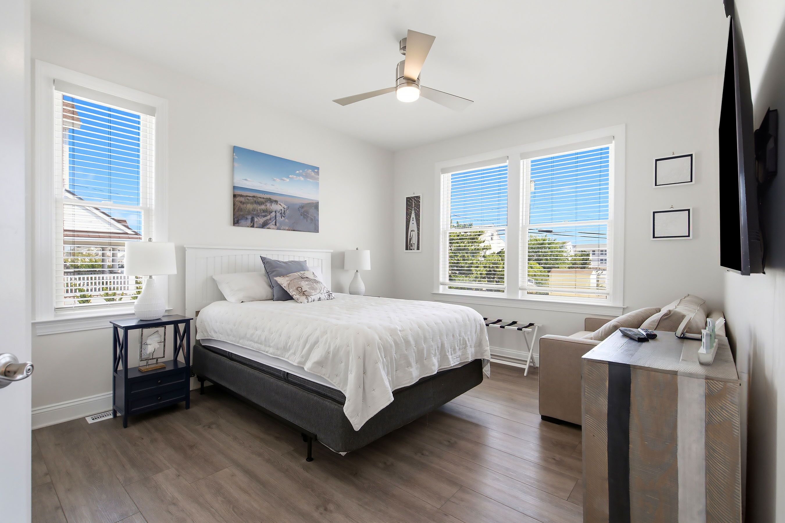 A bedroom with a bed, bedside tables, a ceiling fan, and large windows with blinds.