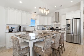 A modern kitchen with white cabinetry, a large island with bar stools, stainless steel appliances, and a view to the outside. - Awesome 5 bed, 5 bath, heated pool - short walk to the beach! (Surf City)
