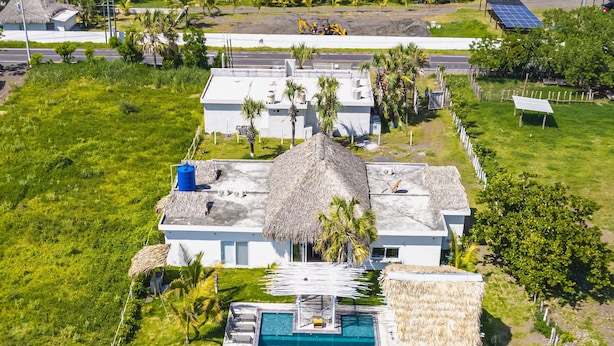 Una casa grande con piscina, rodeada de abundante vegetación y vistas al océano.