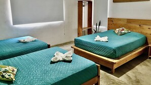 Habitación de hotel con dos camas individuales, cada una con cubrecama color verde agua y una almohada. La cama de la derecha tiene un cabecero de madera, y en la pared izquierda hay una ventana con persianas.