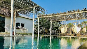 Una piscina con agua cristalina, rodeada de sillas de descanso y hamacas bajo una pérgola.