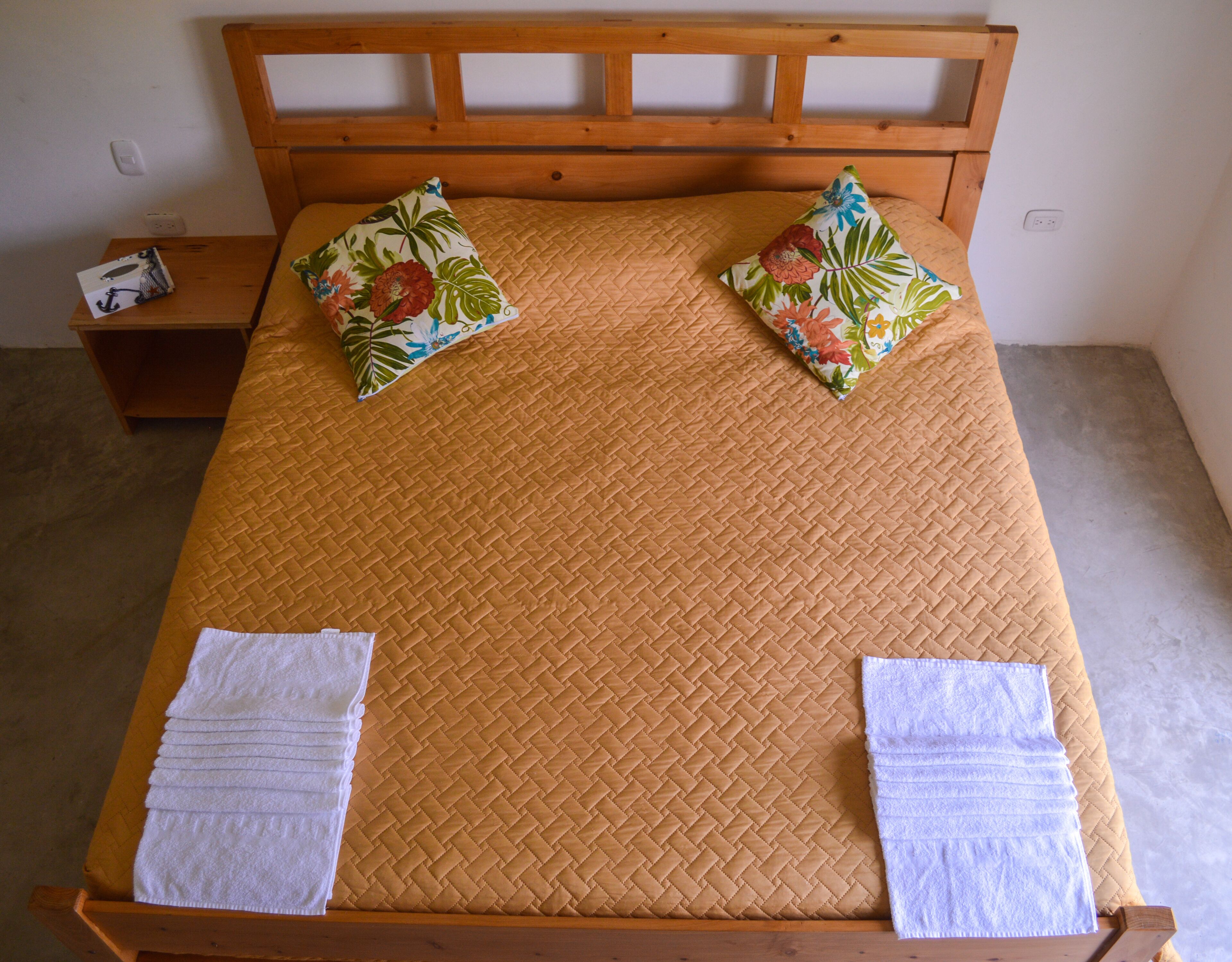 A bed with a wooden headboard, two floral pillows, and two neatly folded white towels.