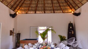 Un comedor con techo de paja, sillas de mimbre blanco y mesa de billar.