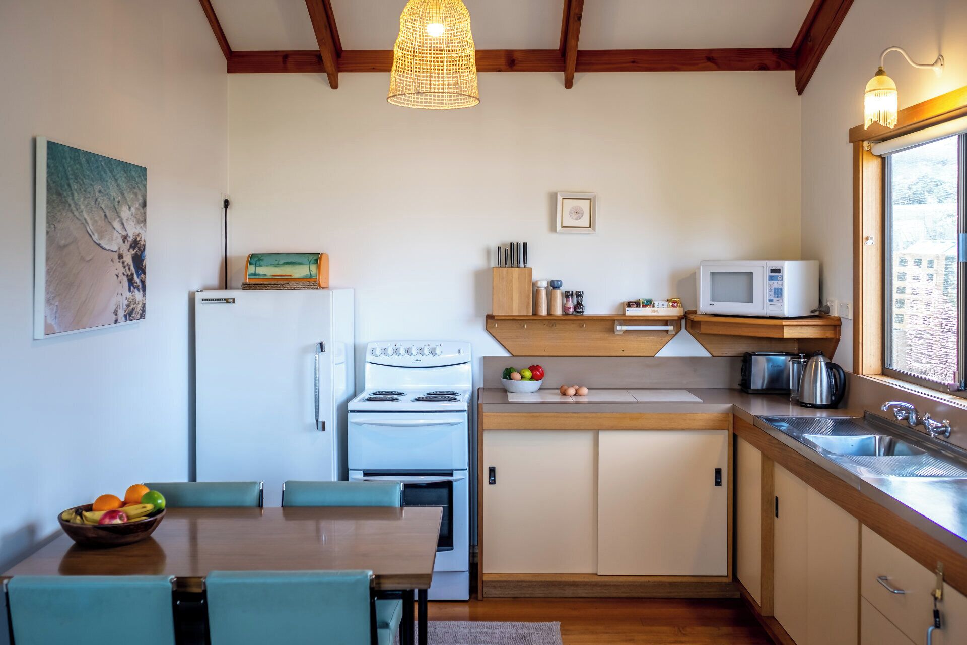 Cocina compacta con refrigerador, estufa, microondas y pileta. Hay una mesa de comedor con sillas y un frutero.
