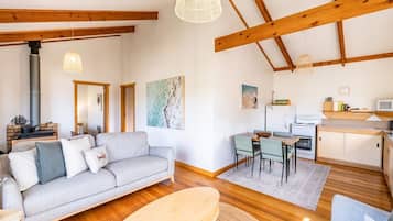 A spacious living area with a sofa, a dining table with chairs, a kitchen area, and a large window.