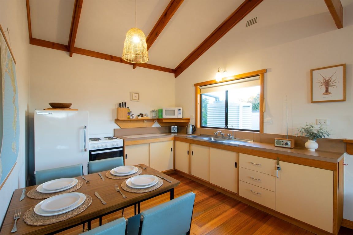 Una cocina compacta con comedor, vigas de madera, lámpara colgante y ventana con persianas.