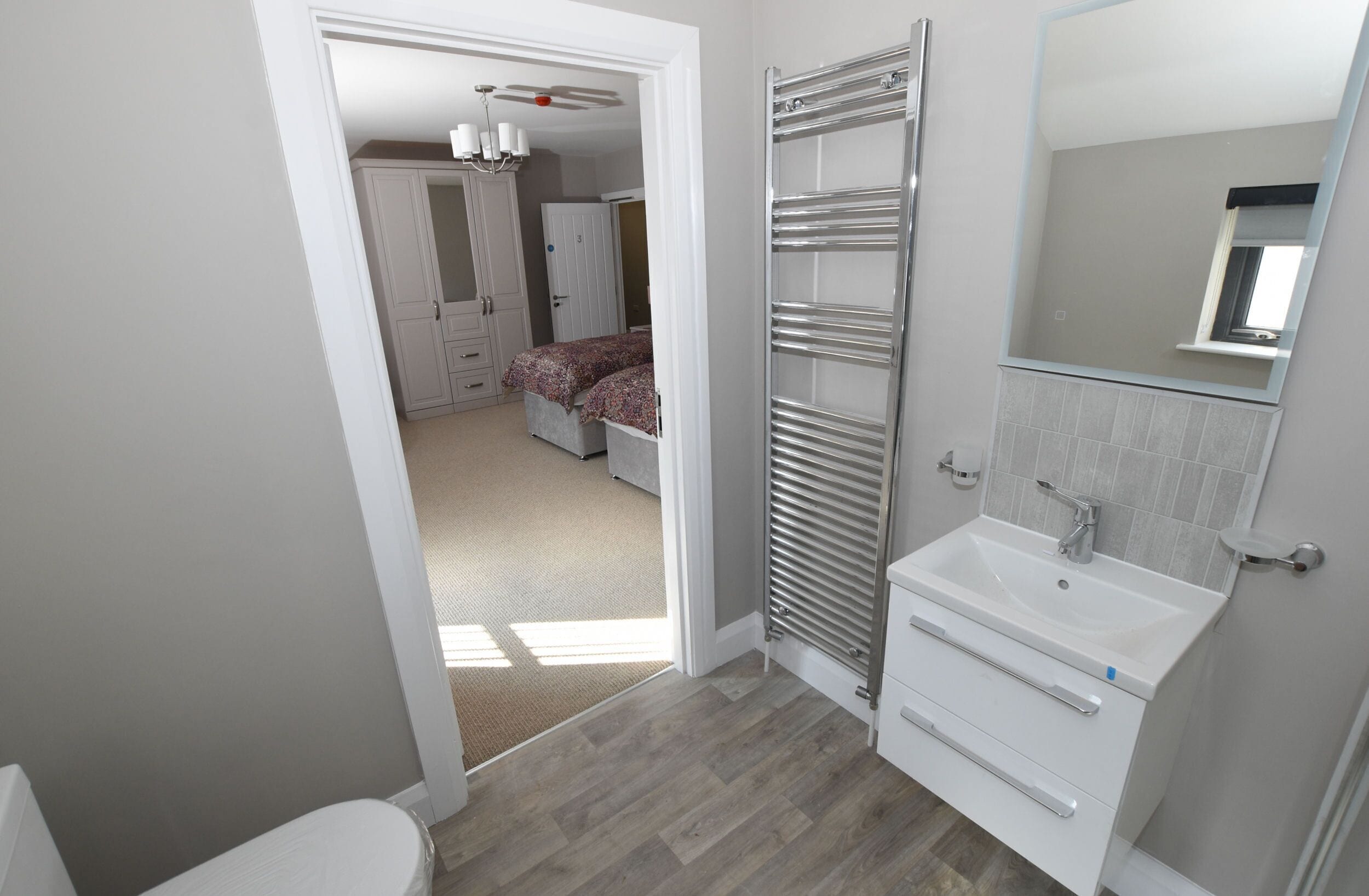 Uma casa de banho moderna com lavat ório branco, espelho e porta-toalhas.
