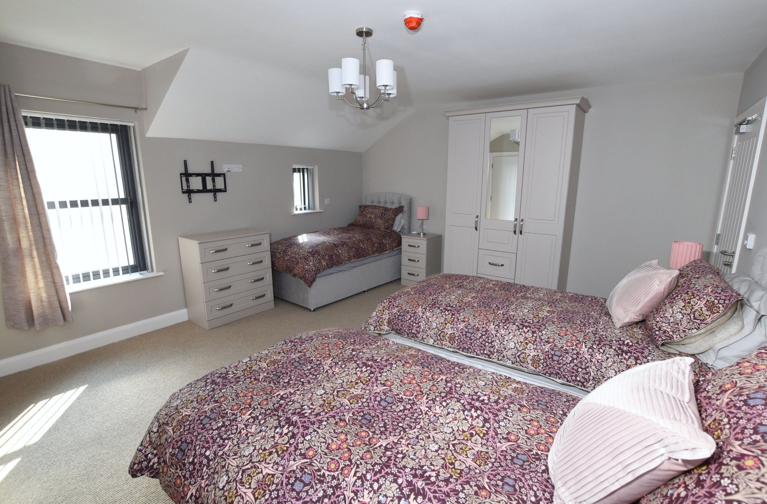 Een slaapkamer met twee bedden, een garderobe, een spiegel en een raam met gordijnen.