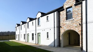 A modern two-story building with a white facade and stone accents, featuring a covered entrance and a well-maintained lawn.