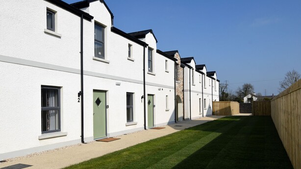 A row of white buildings with green doors, a well-maintained lawn, and a wooden fence.