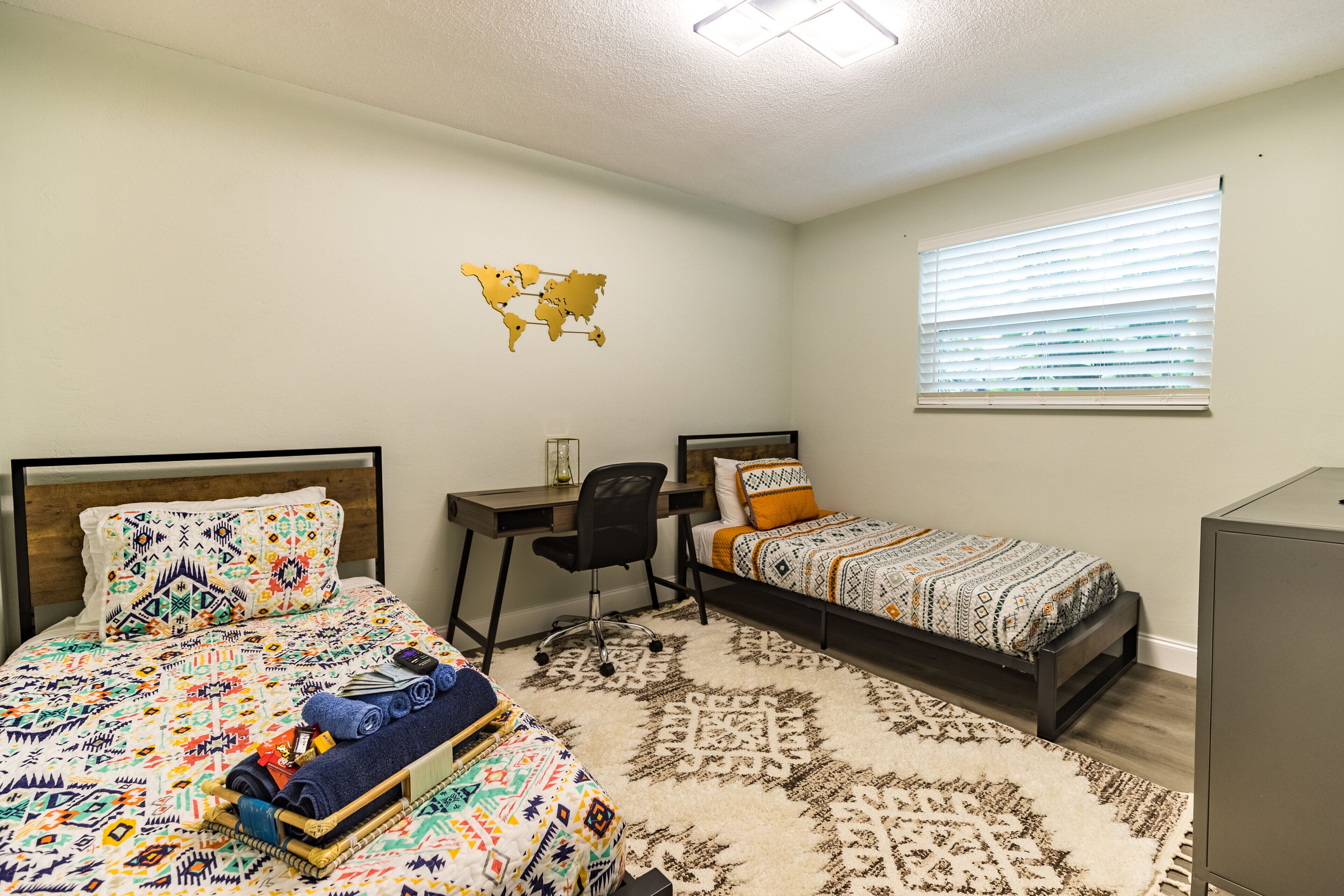 A bedroom with two beds, a desk, a chair, and a map on the wall.