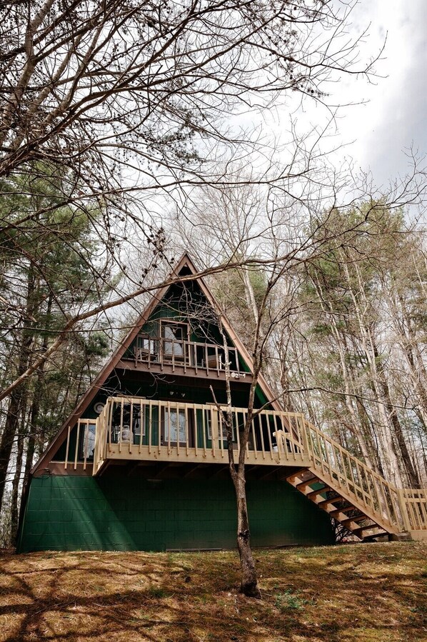 A cabin with a triangular roof, a balcony, and a green exterior wall. - Lazy Lane Cabins - Pleasant View (Logan)