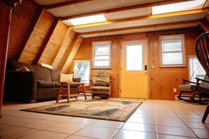 Une pièce mansardée chaleureuse avec un plafond en pente, des murs en bois, un canapé, un fauteuil, une petite table et une porte.