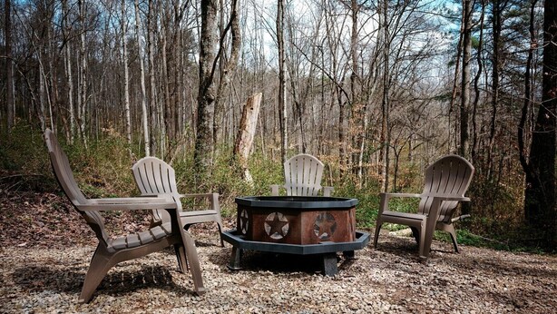Een boslandschap met een vuurplaats en Adirondack stoelen.