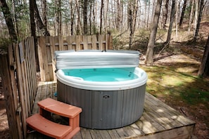 A hot tub on a wooden deck surrounded by a wooden fence, with a small bench nearby.