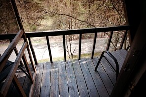 Une terrasse en bois avec une rambarde en métal, donnant sur une zone boisée.