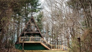 Een chalet met een houten terras en een trap naar een balkon, omgeven door bomen.