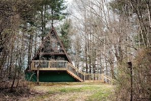 Eine Holzhütte mit einer Holzterrasse und Treppe zu einem Balkon, umgeben von Bäumen.
