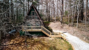 A cabin with a wooden deck and stairs leading to a green-roofed entrance.
