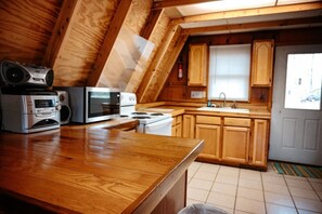 Une cuisine avec des armoires en bois, un four à micro-ondes, une cuisinière et une radio posée sur le comptoir.