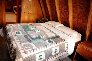 A bedroom with a wooden ceiling, a quilted bedspread, and a wooden nightstand. - Lazy Lane Cabins - Pleasant View (Logan)