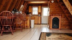 Een knus kamer met zolderkap, voorzien van een open haard, houten balken, een betegelde vloer en een zithoek met stoelen.