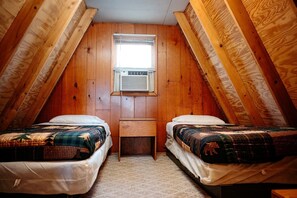 Une petite chambre mansardée avec deux lits, un bureau et une fenêtre.