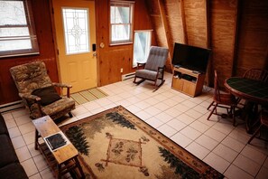 Une pièce chaleureuse avec une porte en bois, un fauteuil à bascule, une télévision et une table à manger avec des chaises.