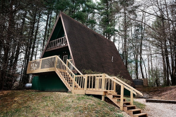 A cabin with a steep roof, wooden staircase, and a green exterior.