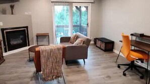 A living room with a fireplace, a sofa, an orange office chair, and a wooden desk. - Cozy contemporary 1-bedroom condo with fireplace (Aurora)