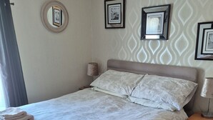 Uma cama bem arrumada com roupa de cama florida, um abajur e uma mesinha de cabeceira de madeira com gavetas.