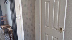 Um corredor com uma porta branca, um espelho e uma parede revestida de azulejos.