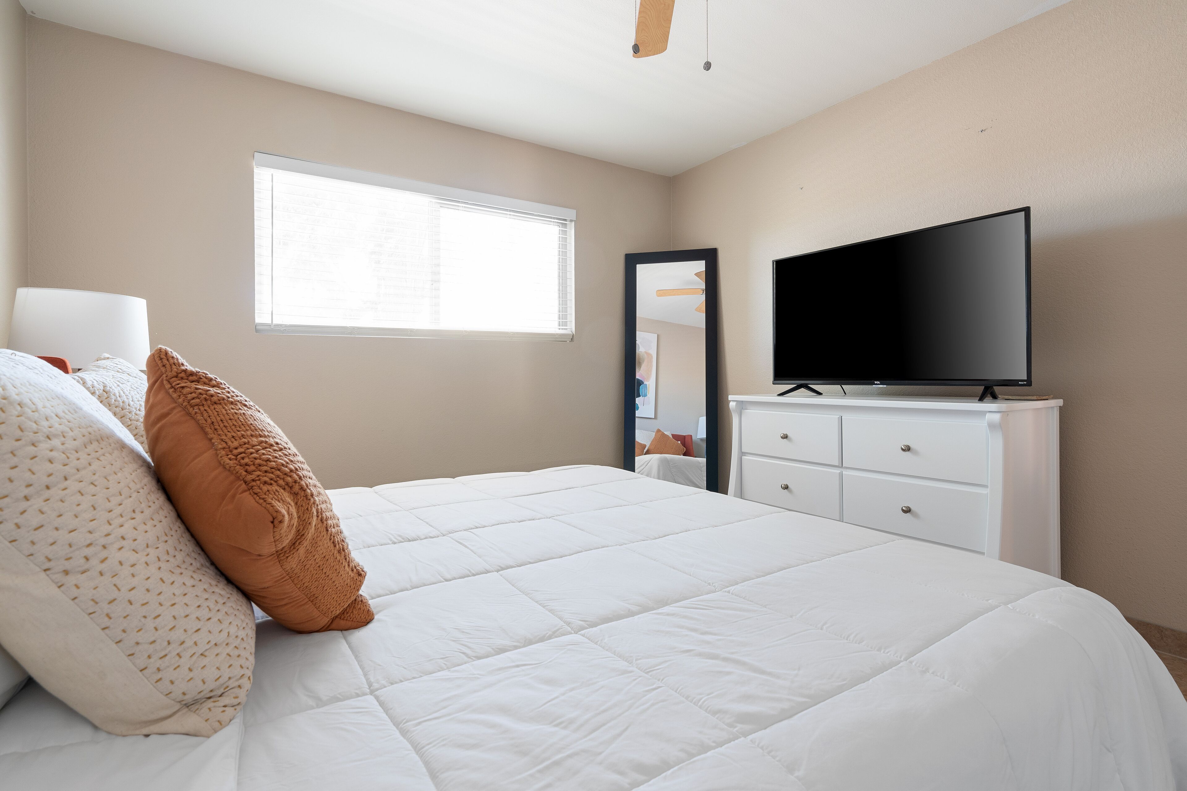 A bedroom with a bed, a TV, a dresser, a window, and a ceiling fan.