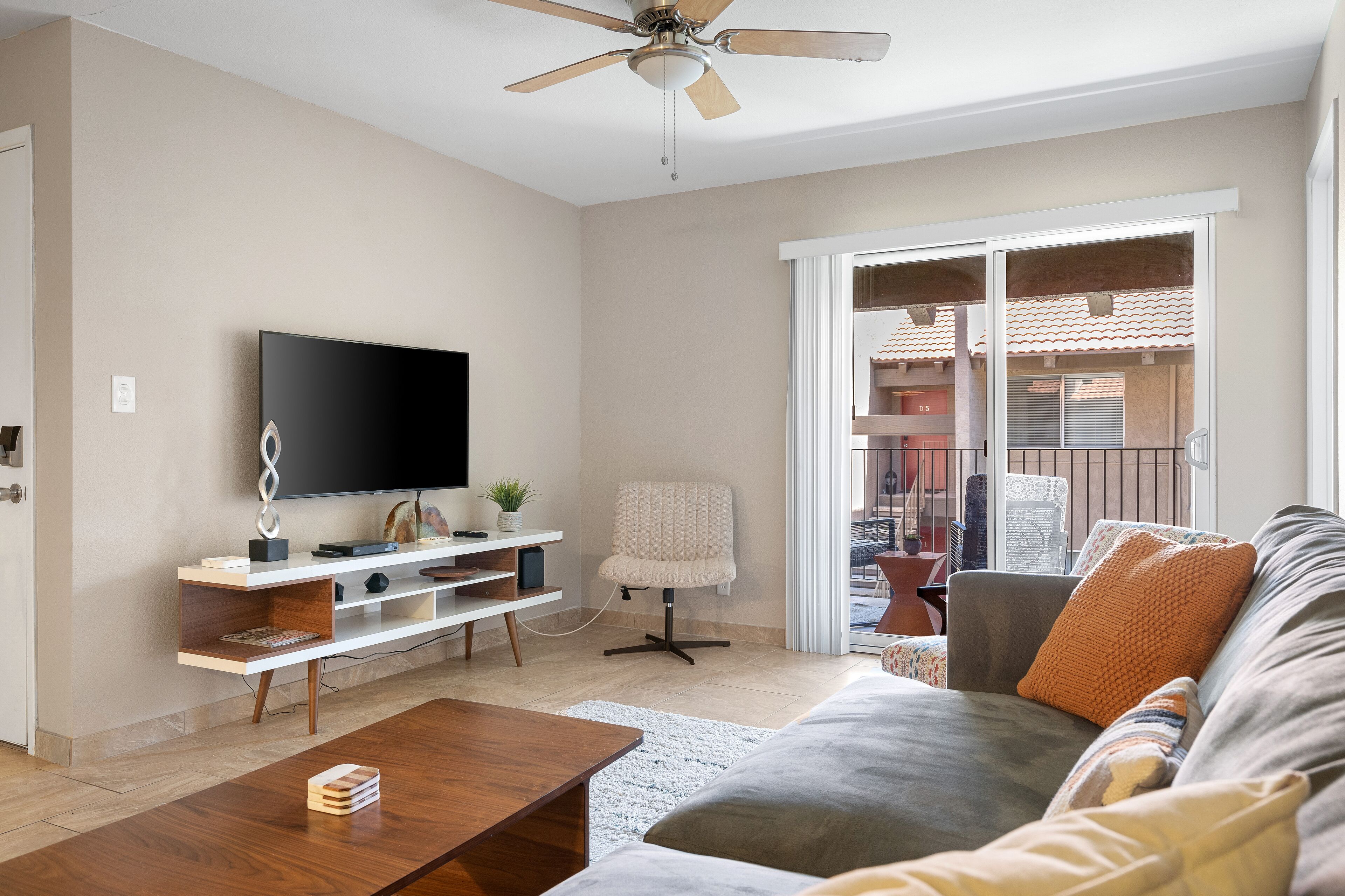 A living room with a flat-screen TV, a wooden coffee table, a grey sofa, and a ceiling fan.