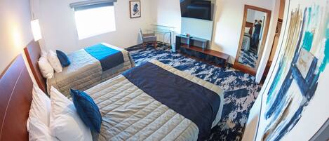 Habitación de hotel con dos camas, un escritorio, una silla, un televisor y un espejo grande.