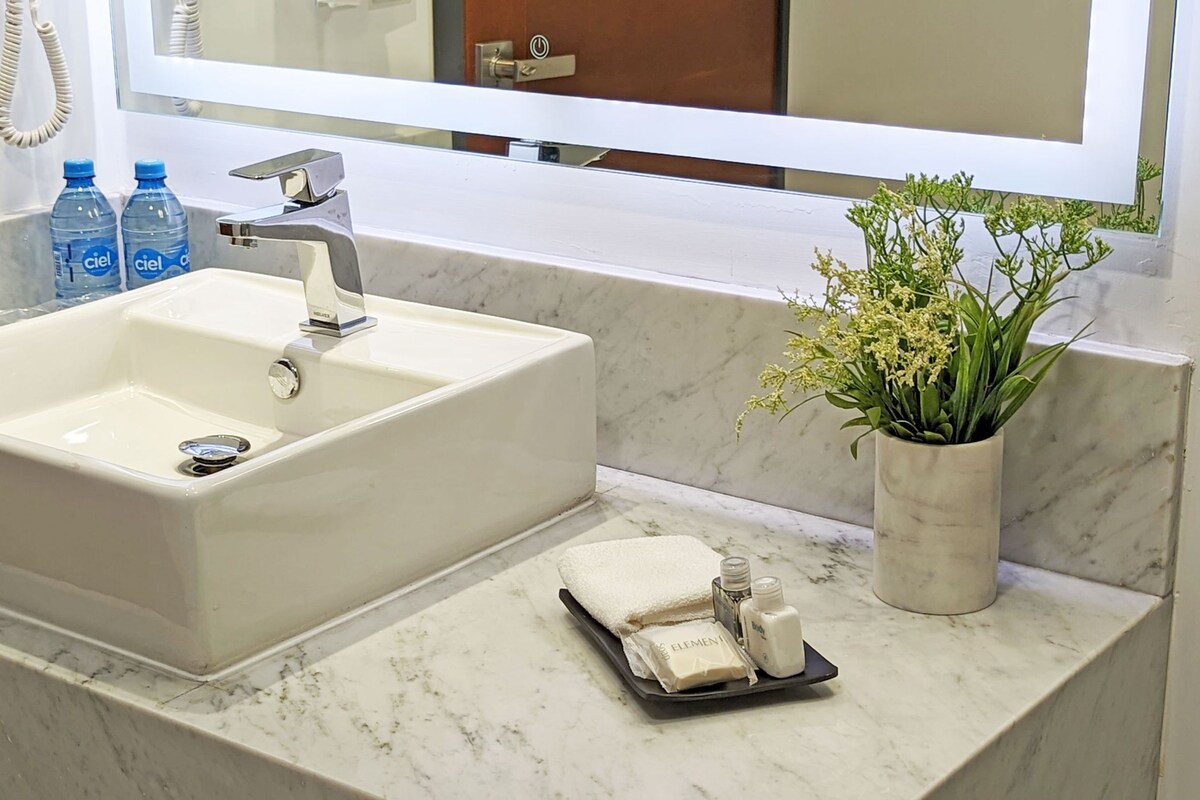 A bathroom with a white sink, a mirror, a potted plant, and toiletries on the counter.