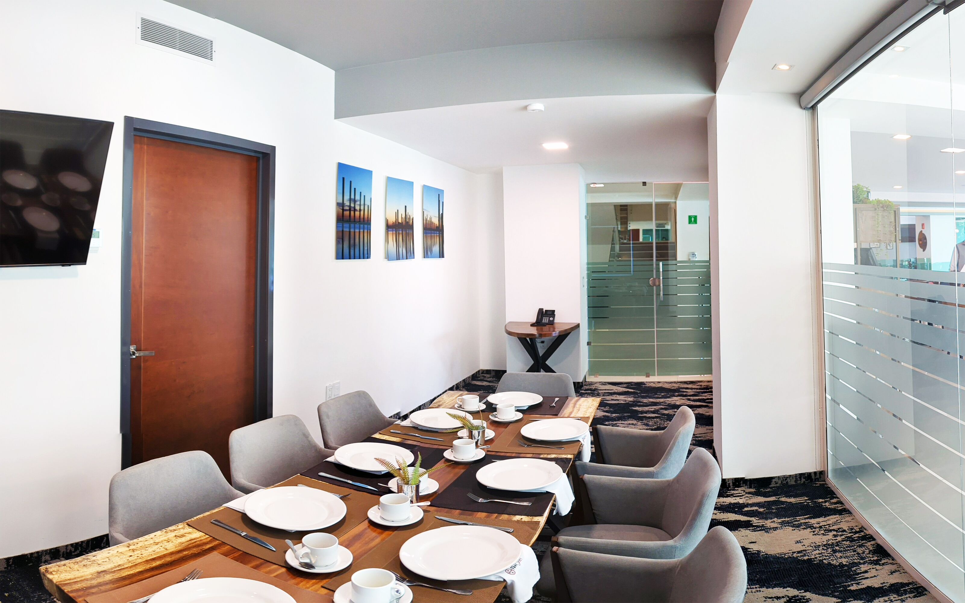 A conference room with a long table set for a meeting, equipped with chairs, plates, cups, and a phone.