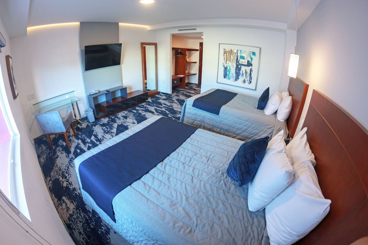 Una habitación de hotel con dos camas, un escritorio, un televisor y un cuadro en la pared.